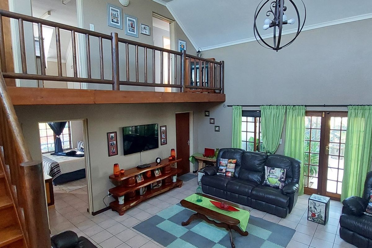 Spacious double-volume living area featuring a timber staircase, mezzanine landing with wooden balustrade, tiled flooring, and direct access to the garden through glass doors.