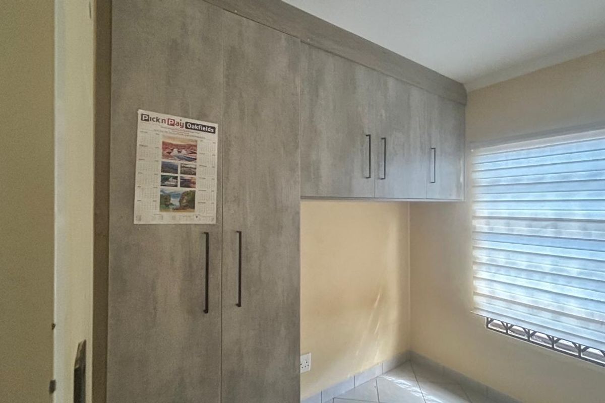 A bedroom featuring built-in grey wood-look cabinetry with overhead storage and a window fitted with modern zebra blinds.