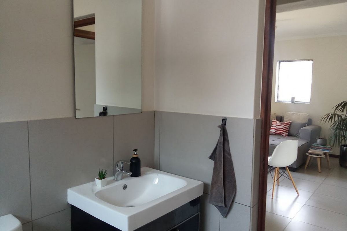 A modern bathroom featuring a vanity with a basin, chrome faucet, and wall-mounted mirror, with a view into the adjacent living area.