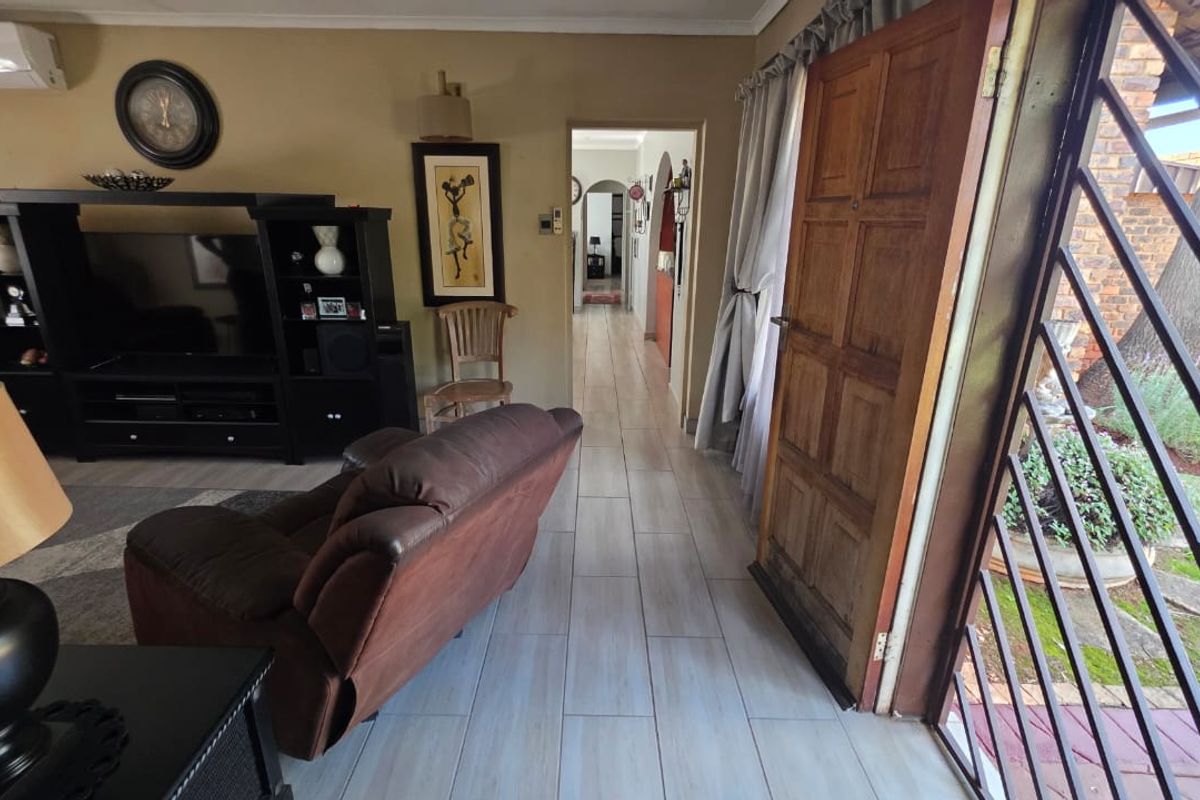 Living room area featuring tiled flooring, a wall-mounted air conditioning unit, and a wooden entrance door with security gate.