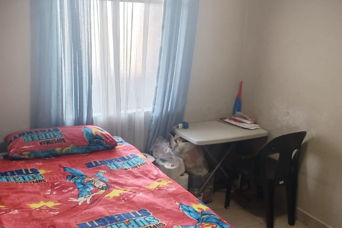 A bedroom featuring tiled flooring and a window with curtains, showing signs of wear on the wall surfaces.