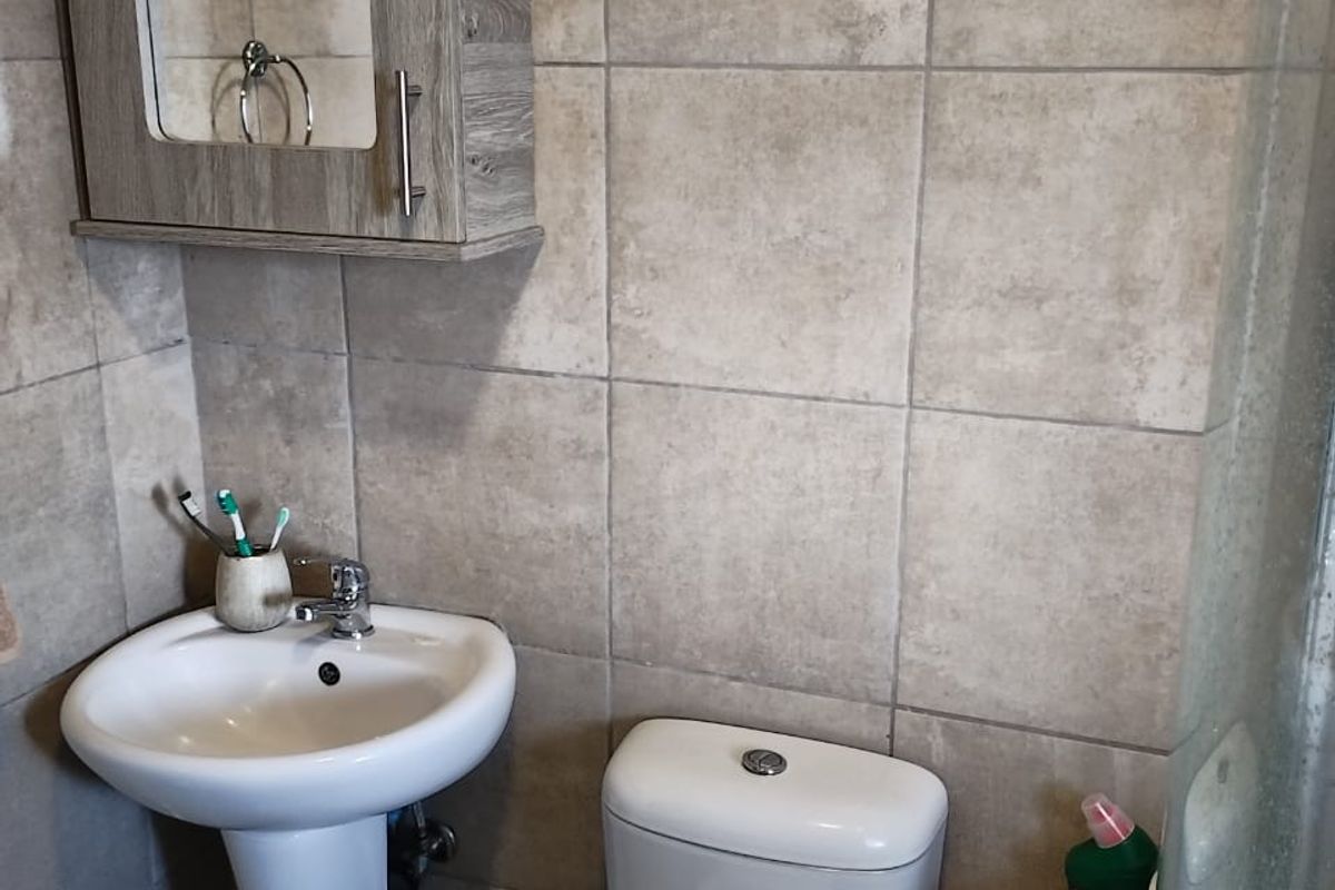 Compact bathroom featuring a pedestal sink, dual-flush toilet, wall-mounted mirrored cabinet, and full-height neutral wall tiling.