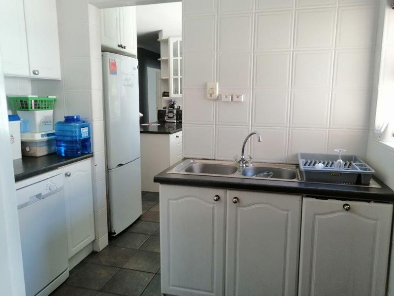 A functional scullery area featuring white cabinetry, dark laminate countertops, a double bowl sink, and tiled splashbacks, providing additional prep and wash-up space.