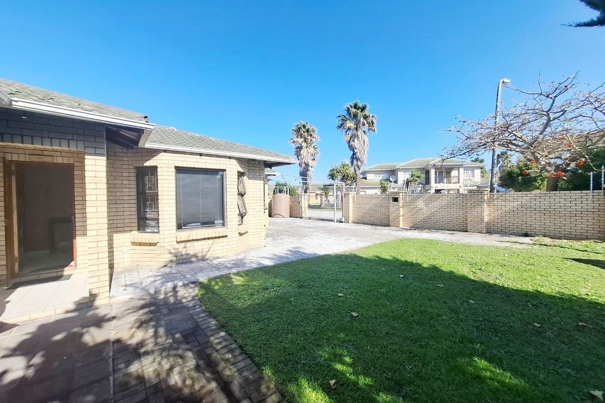 Rear exterior view of the property featuring a face brick facade, paved patio area, well-maintained lawn, and secure perimeter walling.