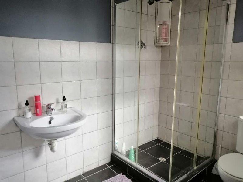 A functional bathroom featuring a wall-mounted basin, a glass-enclosed shower, and a toilet, finished with neutral wall tiles and dark floor tiles.