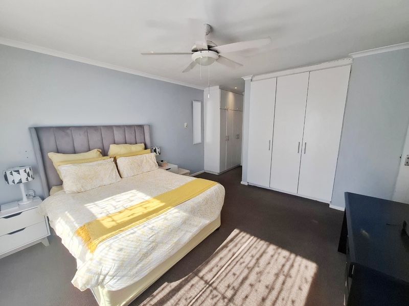 Spacious bedroom featuring neutral wall tones, fitted white built-in cupboards, and a ceiling fan, providing a comfortable and functional living space.