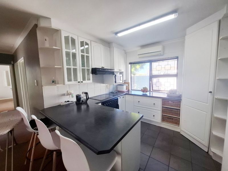 A functional kitchen featuring white cabinetry, dark countertops, an integrated stove with extractor, and a wall-mounted air conditioning unit.