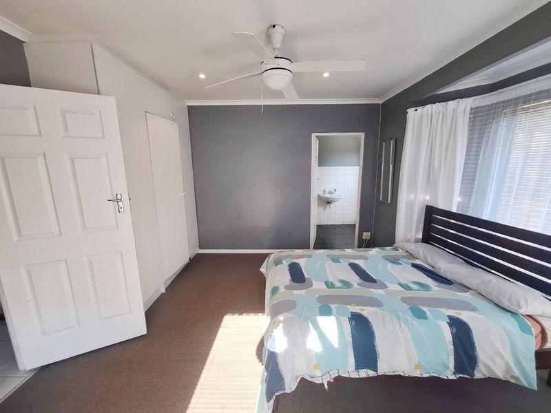 A bedroom featuring built-in cupboards, a ceiling fan, and direct access to an en-suite bathroom with tiled flooring.