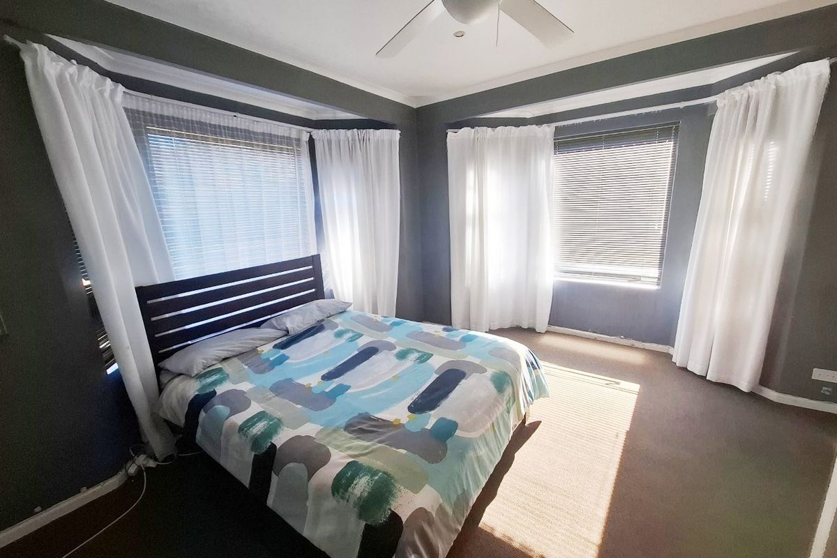 A bedroom featuring dual bay windows with venetian blinds, a ceiling fan, and dark grey walls with white trim.