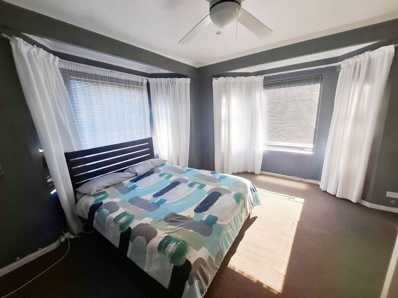 A bedroom featuring dual bay windows with venetian blinds, a ceiling fan, and dark grey walls with white trim.
