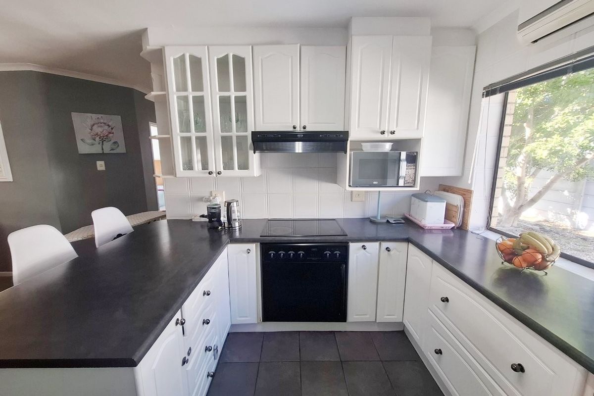 A functional kitchen featuring white cabinetry, dark countertops, integrated appliances including an oven and hob, and tiled flooring with an adjacent breakfast bar.