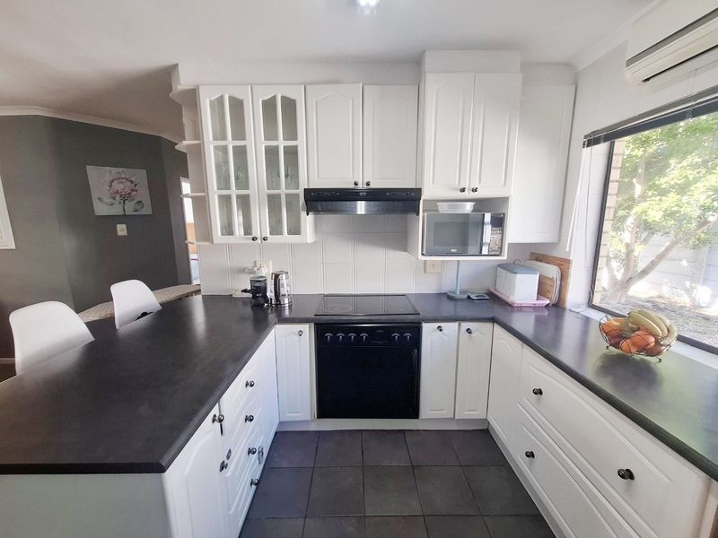 A functional kitchen featuring white cabinetry, dark countertops, integrated appliances including an oven and hob, and tiled flooring with an adjacent breakfast bar.