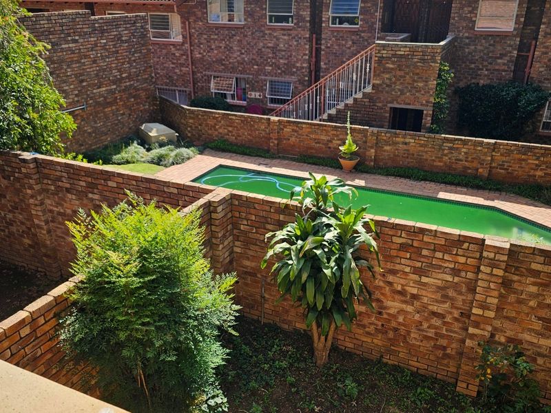 Rear view of the apartment complex featuring a private swimming pool, brick boundary walls, and communal garden space.