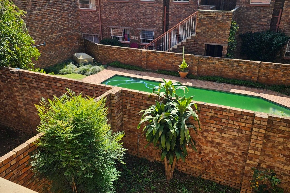 Rear view of the apartment complex featuring a private swimming pool, brick boundary walls, and communal garden space.