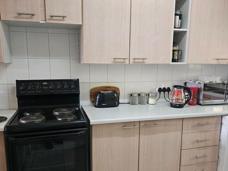 A functional kitchen featuring light wood-tone cabinetry, a tiled backsplash, laminate countertops, and a black freestanding electric stove with an oven.
