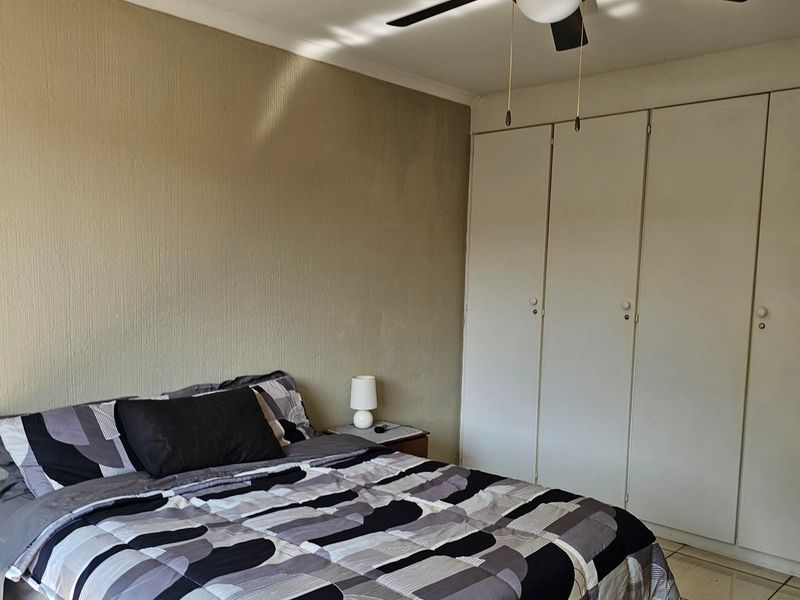 A bedroom featuring built-in cupboards, a ceiling fan, and tiled flooring, offering a functional space with neutral wall finishes.