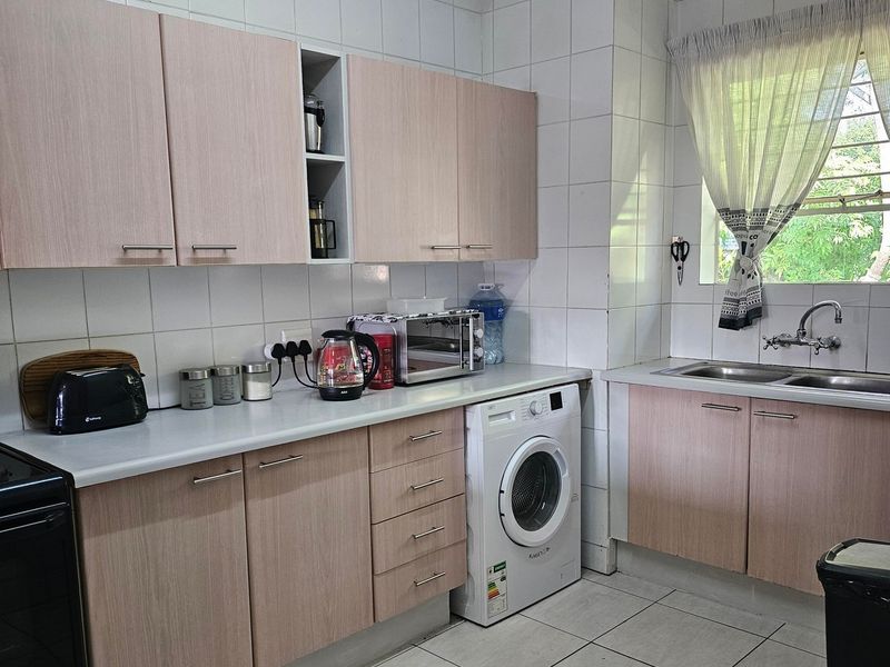 Functional kitchen featuring light wood-look cabinetry, tiled splashbacks, double stainless steel sink, and integrated space for a washing machine.