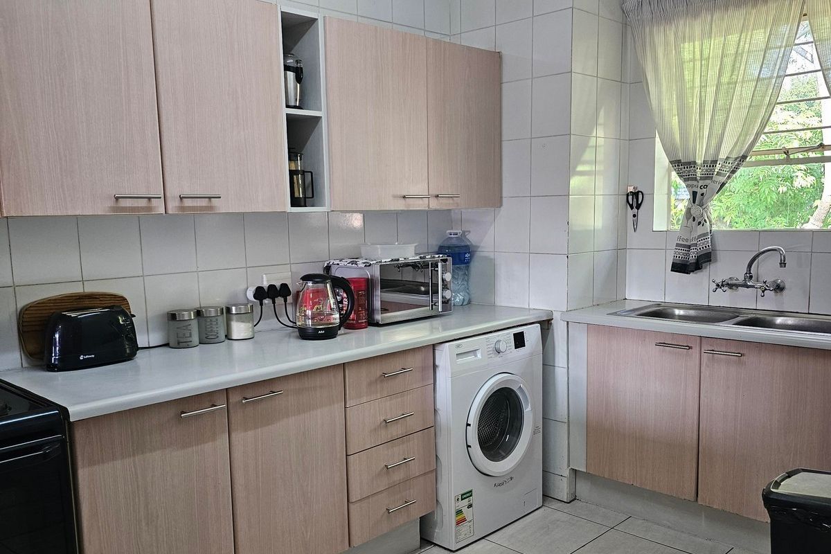 Functional kitchen featuring light wood-look cabinetry, tiled splashbacks, double stainless steel sink, and integrated space for a washing machine.