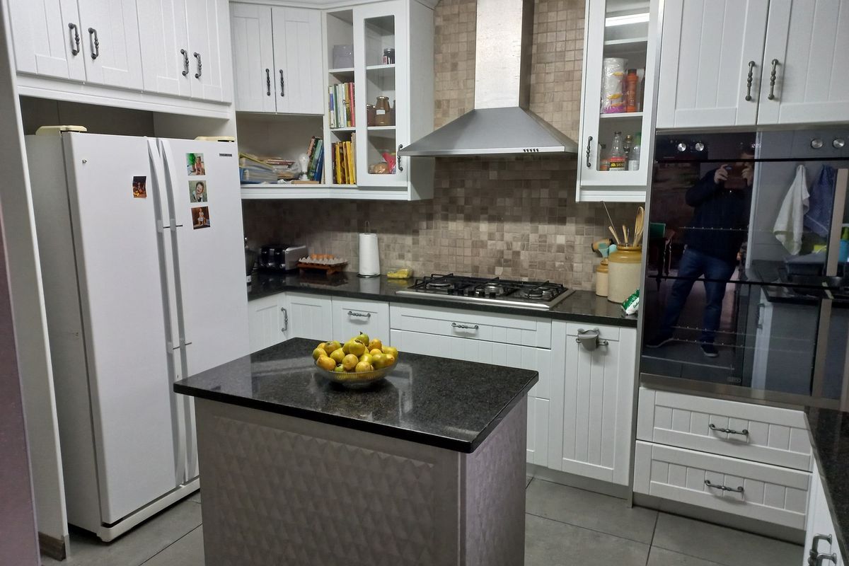 A well-appointed kitchen featuring white cabinetry, granite countertops, a central island, stainless steel extractor fan, and a built-in oven with tiled backsplash.