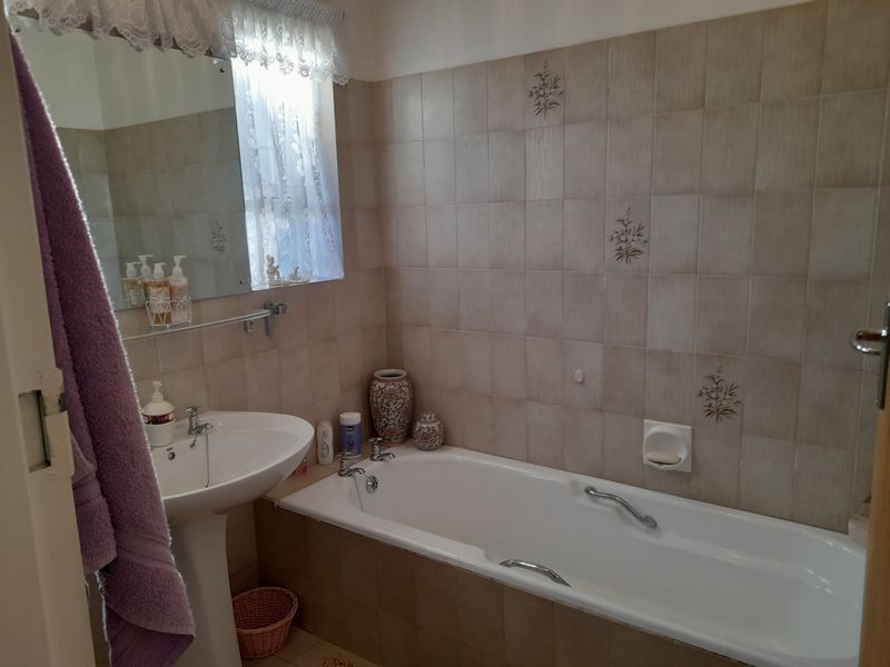 A functional bathroom featuring a pedestal washbasin, a standard bathtub, and neutral ceramic wall tiling.