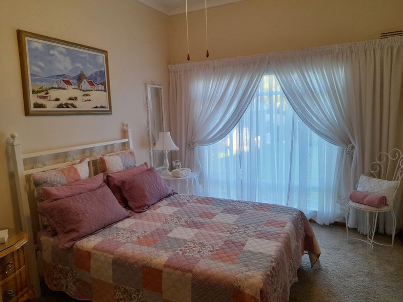 A cozy bedroom featuring carpeted flooring, a ceiling fan, and a large window with sheer curtains allowing natural light.