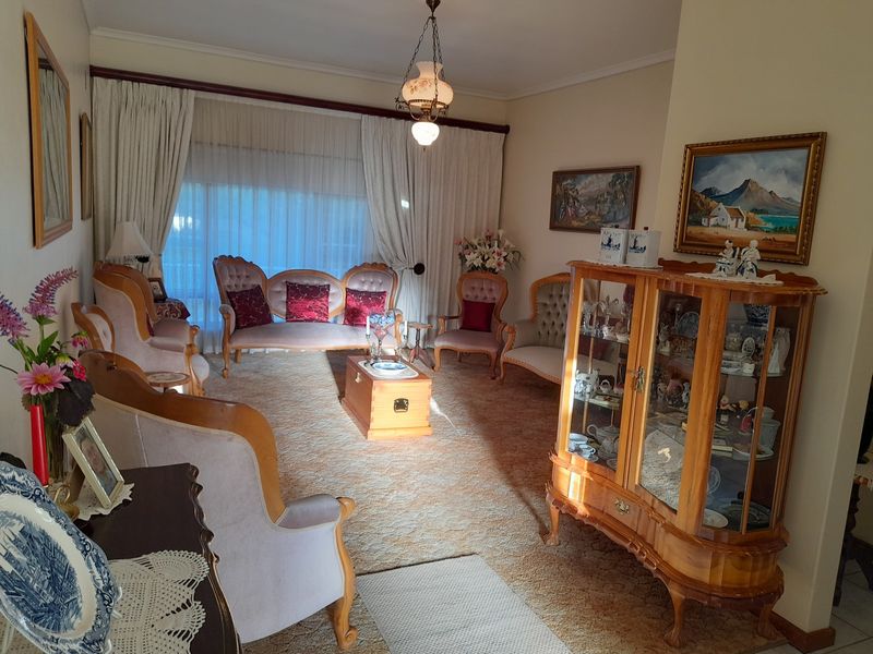 A traditional living room featuring carpeted flooring, large window curtains, and a central pendant light fixture, offering a classic and well-maintained living space.