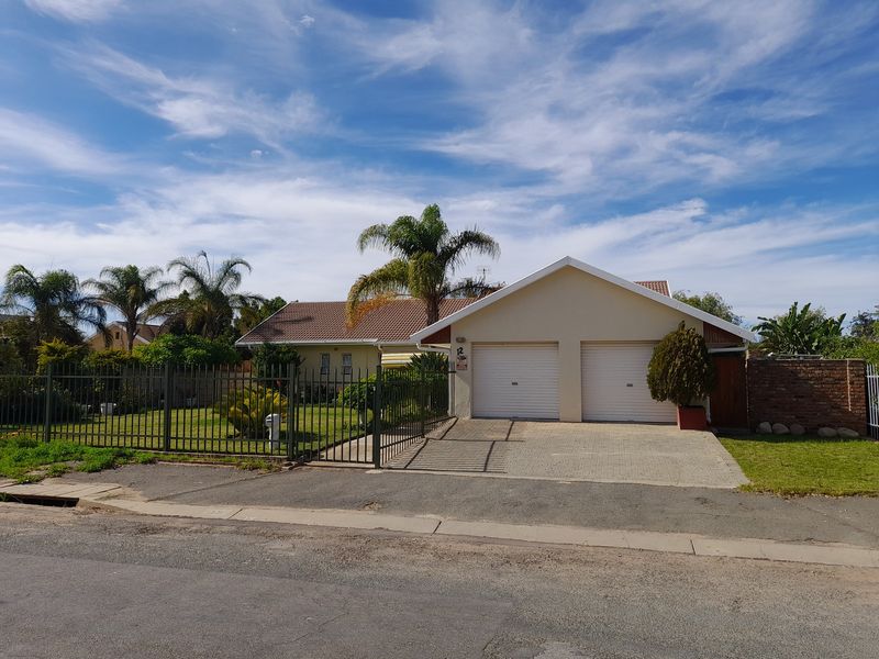 Front view of a residential property featuring a double garage, paved driveway, and established garden enclosed by metal perimeter fencing.