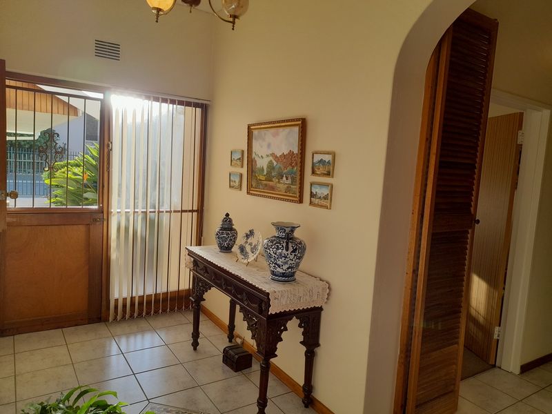 A bright entrance hall featuring tiled flooring, an arched doorway leading to adjacent rooms, and a louvered wooden door with vertical blinds.