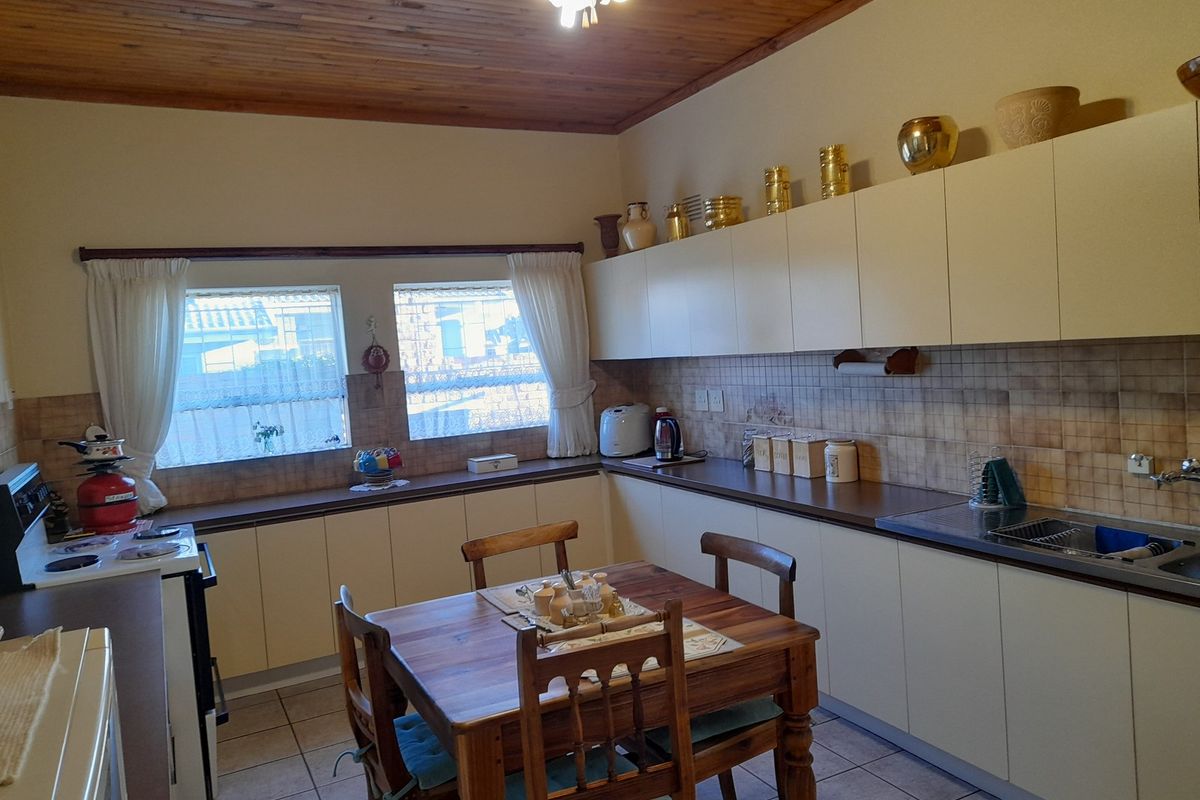 A functional kitchen featuring timber ceilings, tiled splashbacks, laminate countertops, and ample built-in cabinetry with a dedicated dining area.