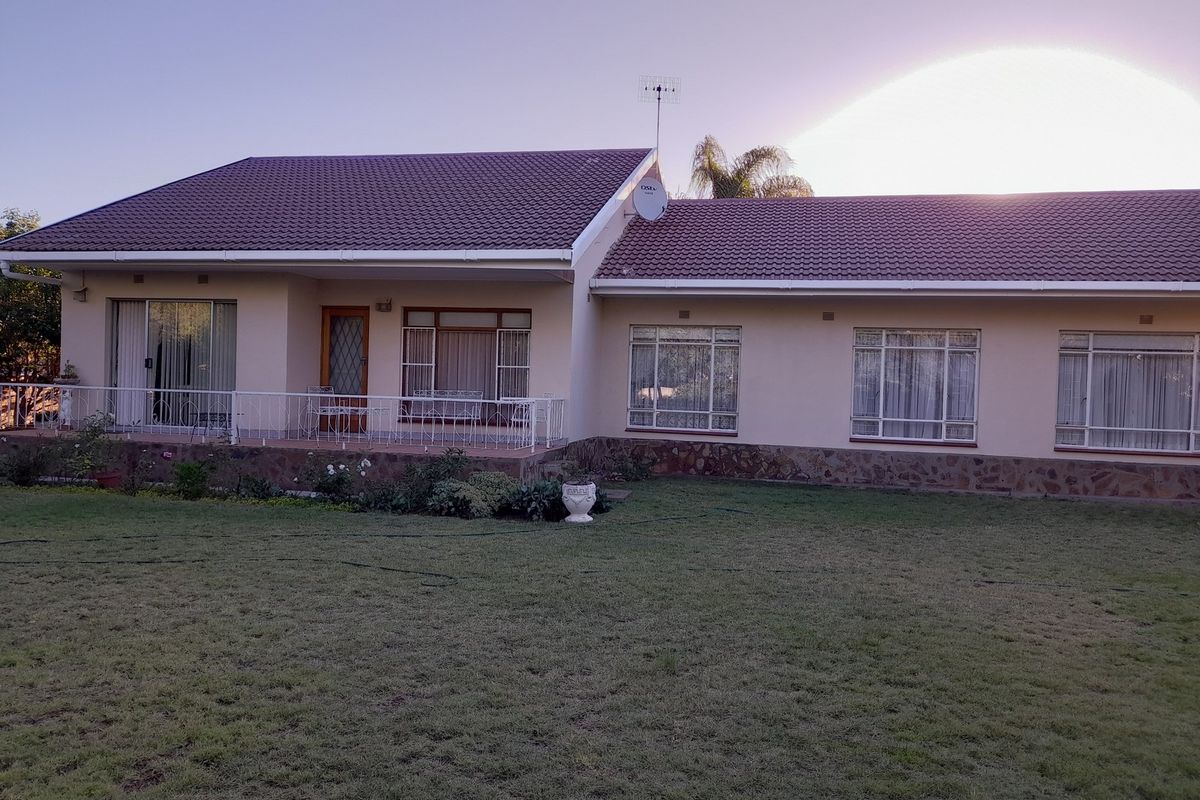 A rear view of a single-story house featuring a tiled roof, stone-clad base, and a covered patio overlooking a spacious lawn.