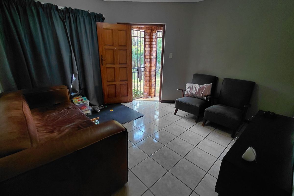 A living room featuring tiled flooring and direct access to an outdoor area through a wooden door with security gate.