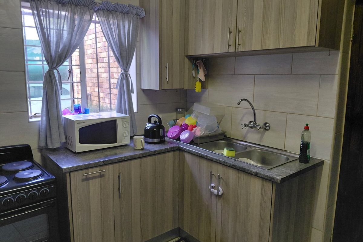 A functional kitchen featuring wood-grain cabinetry, a double stainless steel sink, tiled splashbacks, and a built-in stove with an oven.