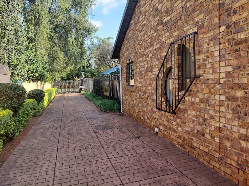 A side view of the property featuring a paved driveway, face brick exterior walls, and secure metal perimeter fencing.