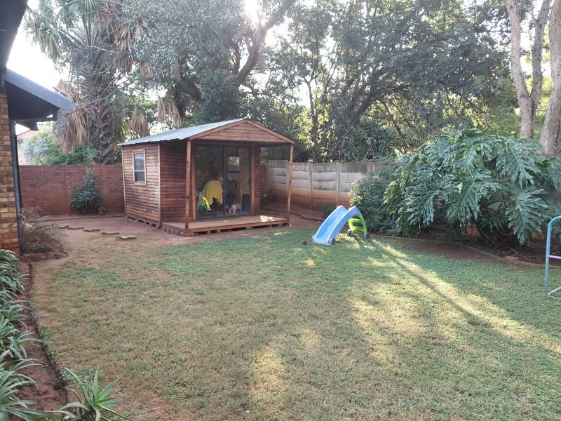A spacious backyard featuring a wooden cabin, established trees, and a mix of brick and precast concrete boundary walls.