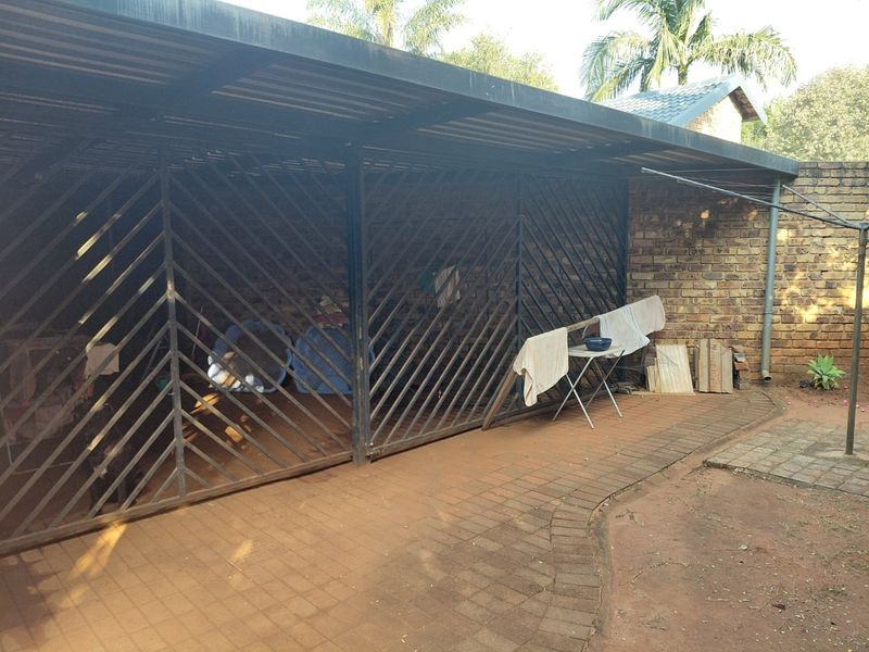 A covered outdoor parking area or garage structure featuring a metal security gate and brick wall construction with paved flooring.