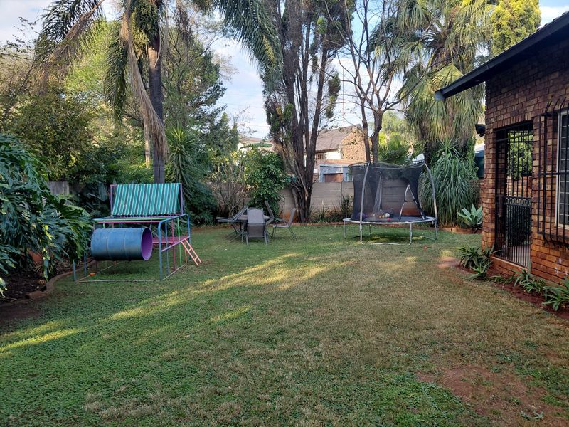 A view of the rear garden featuring a lawn area, mature trees, and a brick exterior wall with security bars on the windows.