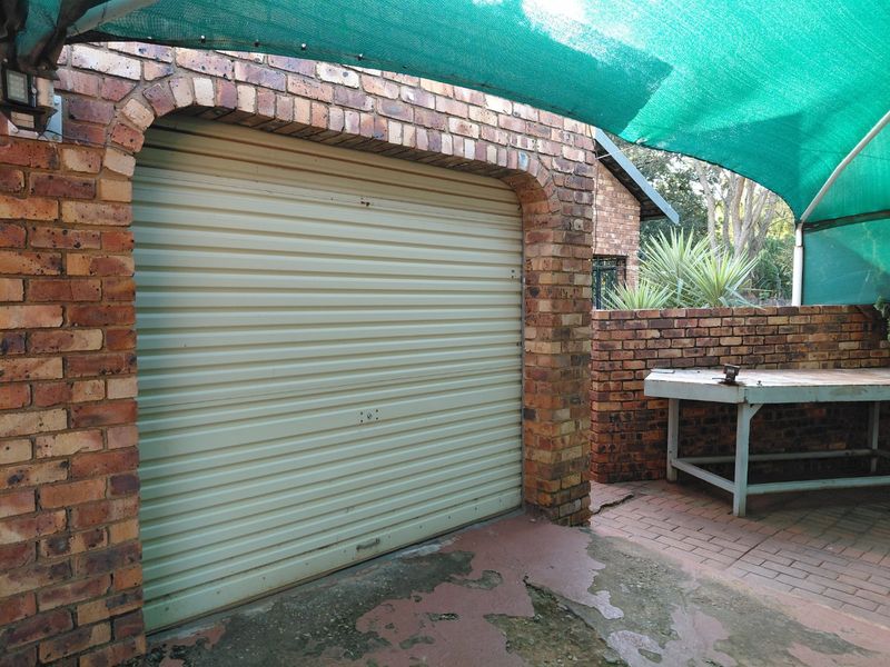 Exterior view of a brick garage featuring a roller door, paved area, and a shade cloth canopy structure.