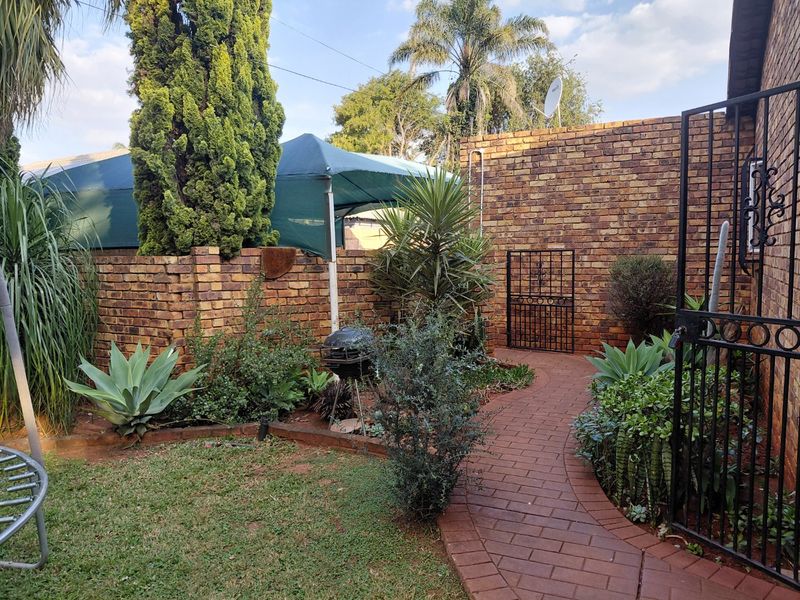 A private garden area featuring a brick paved pathway, established landscaping, and secure brick boundary walls with a wrought iron gate.