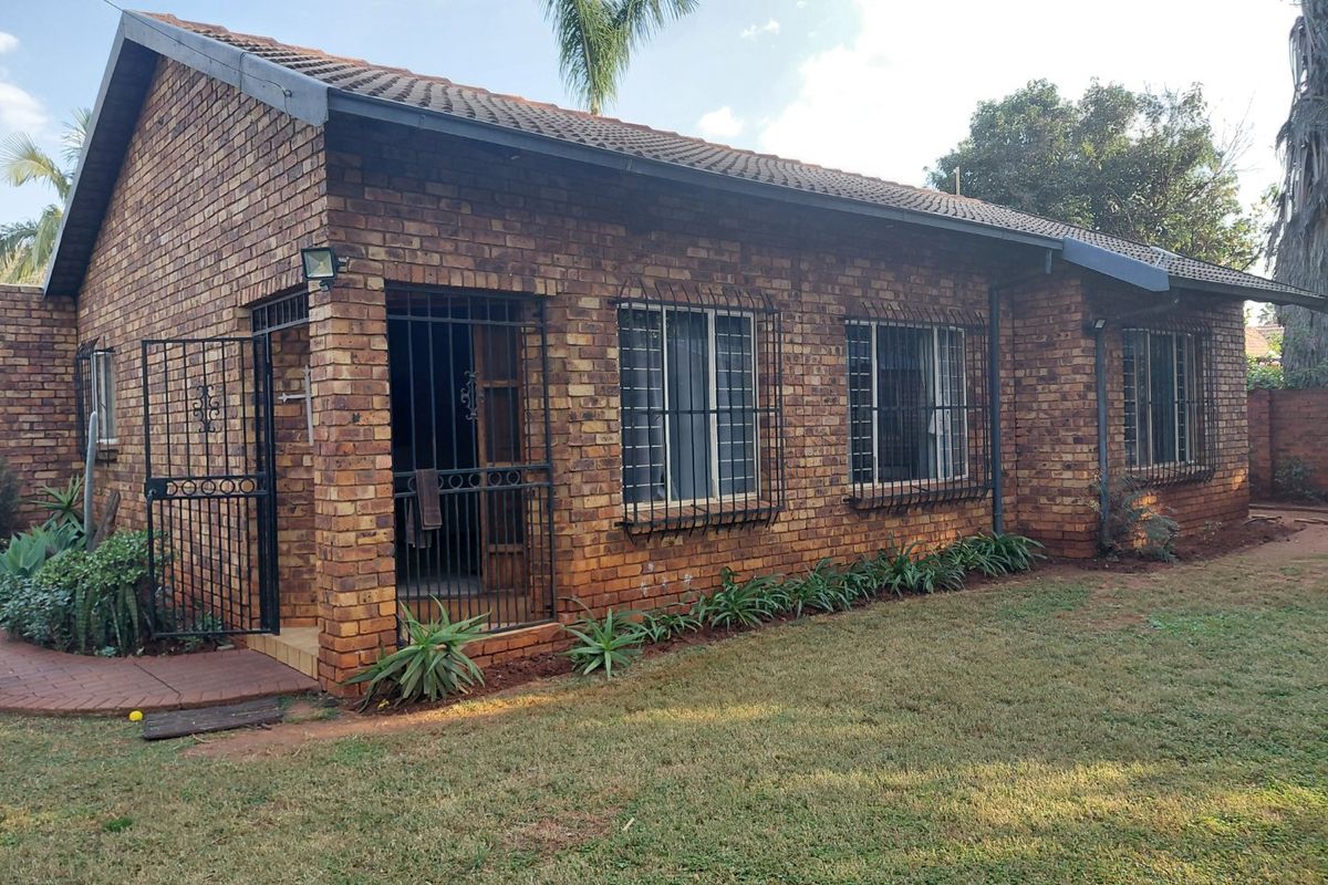 A view of the rear exterior of a face brick house featuring a tiled roof, security bars on windows, and a paved walkway.