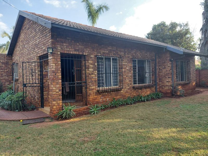 A view of the rear exterior of a face brick house featuring a tiled roof, security bars on windows, and a paved walkway.