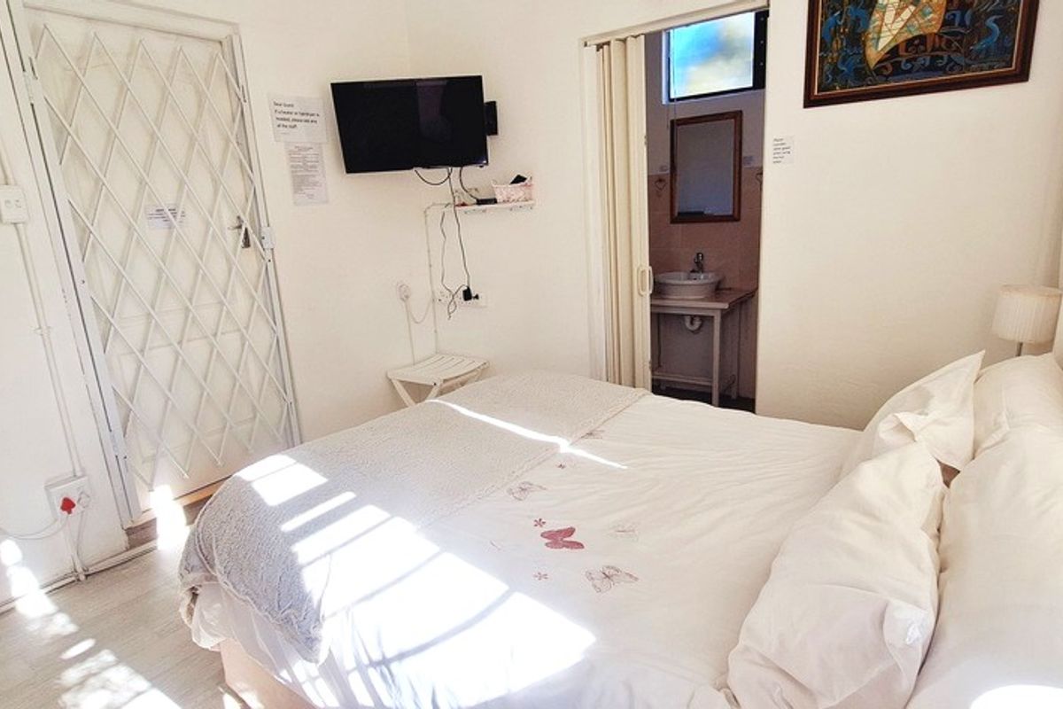 A compact bedroom featuring a built-in security gate, laminate flooring, and an en-suite bathroom with a pedestal basin.