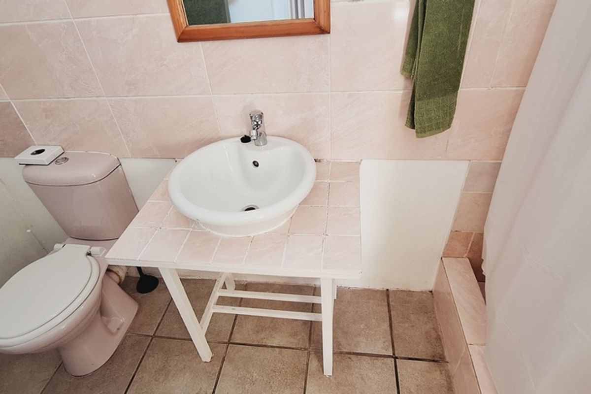A compact bathroom featuring a pedestal-style vanity with a ceramic basin, a standard toilet, and a tiled shower area with a curtain.