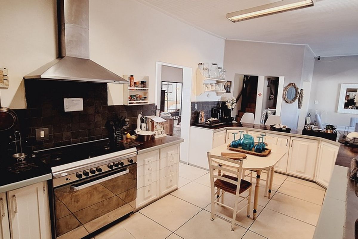 A functional kitchen featuring a stainless steel extractor fan, built-in oven, tiled backsplash, and ample cabinetry, flowing into an adjacent living area.