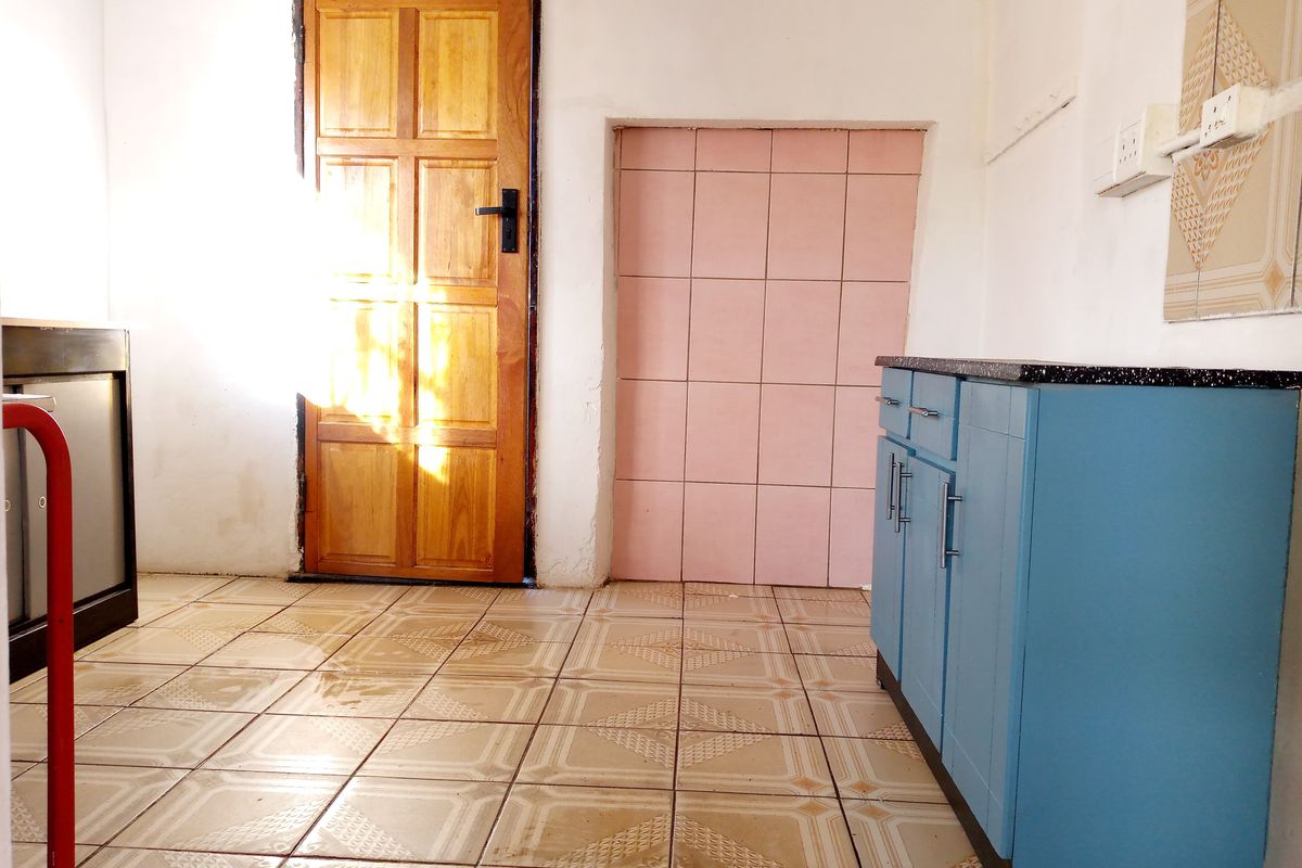 A functional kitchen area featuring blue cabinetry, tiled flooring, and a wooden door, offering a basic layout for culinary activities.