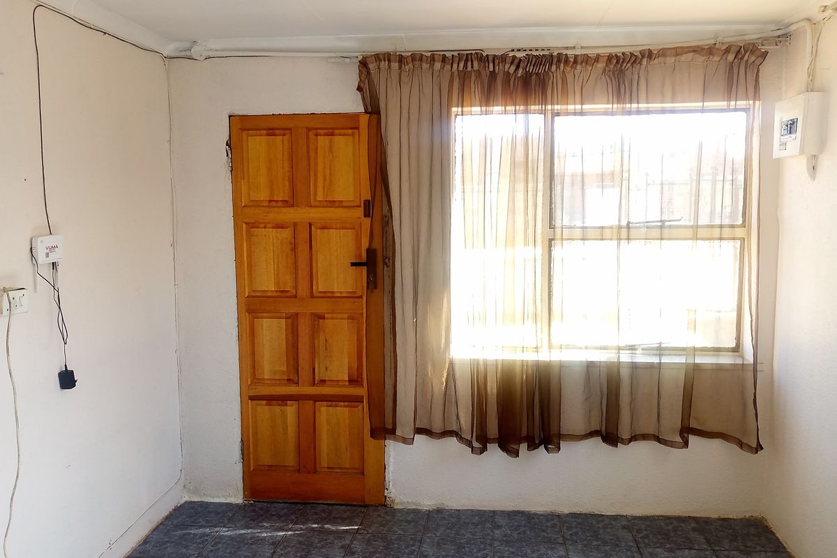 A basic interior room featuring tiled flooring, a wooden panel door, and a window with curtaining, suitable for renovation or restyling.