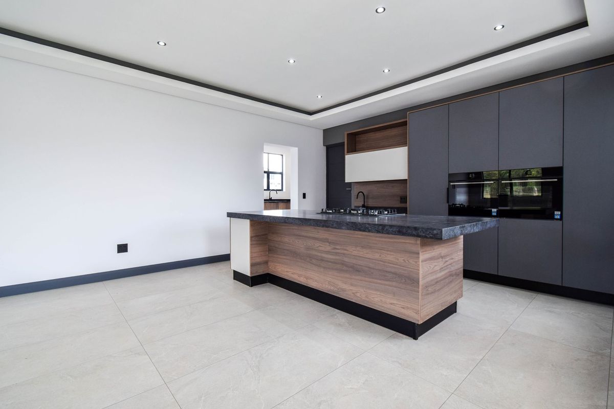 Modern kitchen featuring a central island with a built-in gas hob, sleek dark cabinetry, integrated ovens, and large format floor tiles.