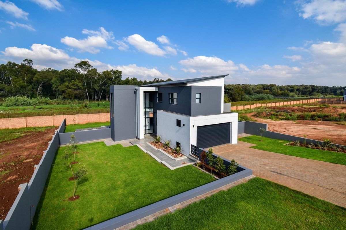 Aerial view of a modern double-story house featuring a paved driveway, double garage, landscaped lawn, and perimeter boundary walls.
