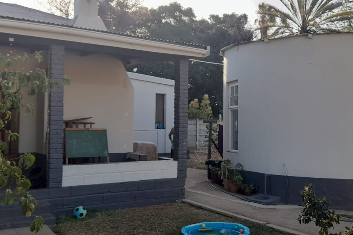 A view of the rear exterior featuring a covered patio area and a secondary circular structure with painted masonry walls.