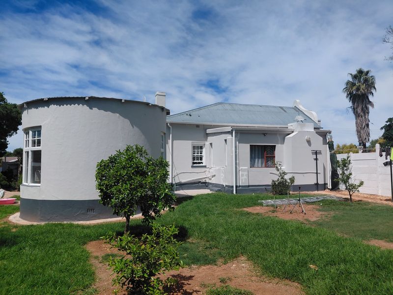 Rear view of the property featuring a unique circular architectural extension, corrugated metal roofing, and a private garden area with boundary walling.