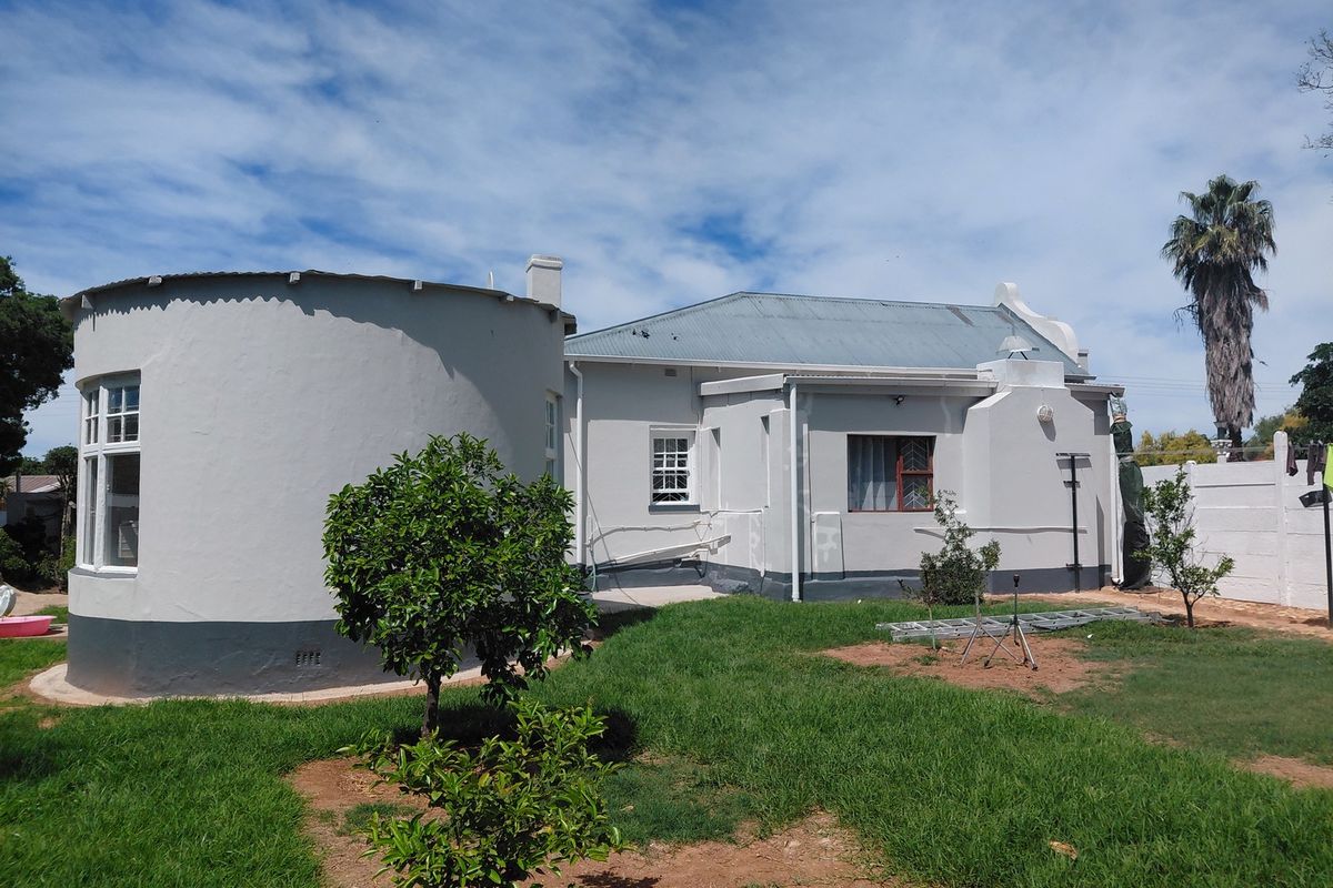 Rear view of the property featuring a unique circular architectural extension, corrugated metal roofing, and a private garden area with boundary walling.